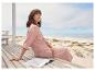 Femme relaxant en tenue rose sur une terrasse en bois, près de la mer.