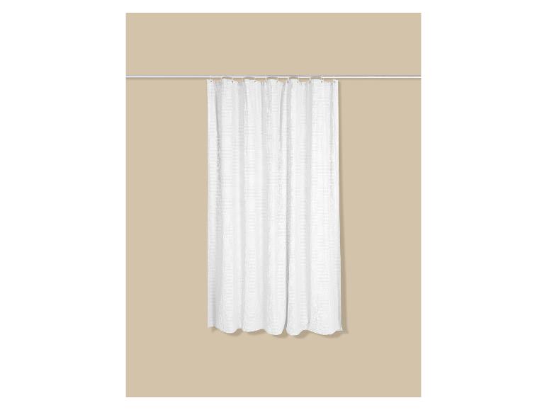 Rideau de douche blanc suspendu sur un mur beige.