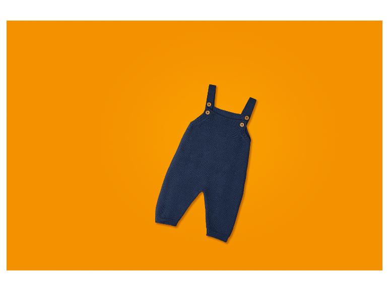 Salopette en tricot bleu foncé pour bébé avec bretelles et boutons en bois, sur fond orange.