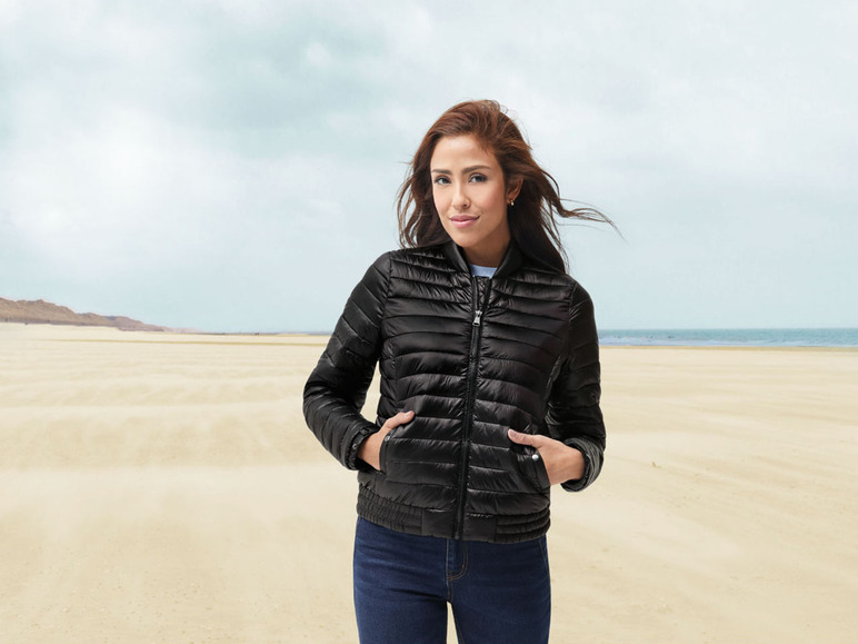Une femme portant une veste matelassée noire sur la plage.