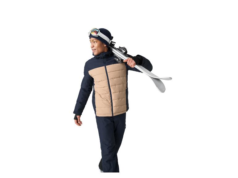Homme en veste et pantalon de ski avec des skis sur l'épaule