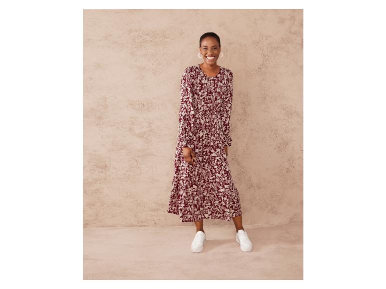 Une femme porte une longue robe rouge à imprimé floral blanc et des baskets blanches.