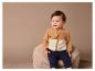 Un bébé portant une veste en polaire marron et un pantalon bleu foncé, assis sur un pouf en fourrure.