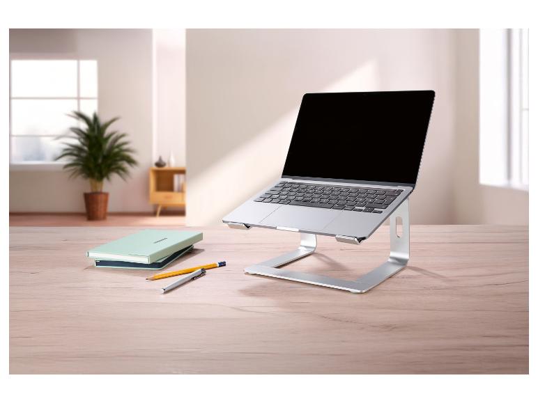 Support d'ordinateur portable argenté avec un ordinateur portable, des carnets et des stylos sur une table en bois.