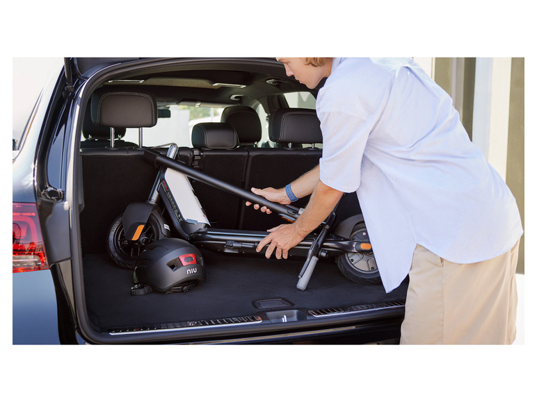 Un homme range une trottinette électrique NIU et un casque dans le coffre d'une voiture.