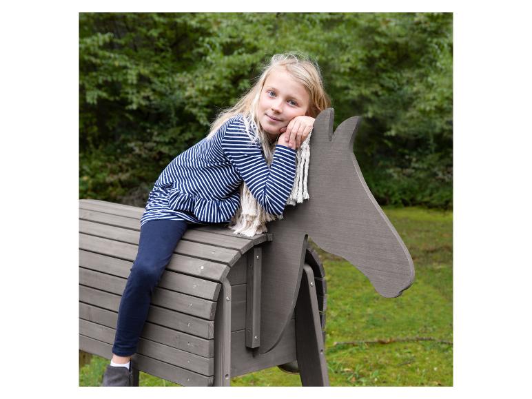 Fille blonde assise sur un cheval jouet en bois à l'extérieur.