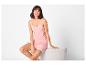 Femme en pyjama rose avec de la dentelle, assise sur fond blanc.