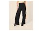 Femme en pantalon noir large, haut jaune et sandales noires, avec un sac beige.