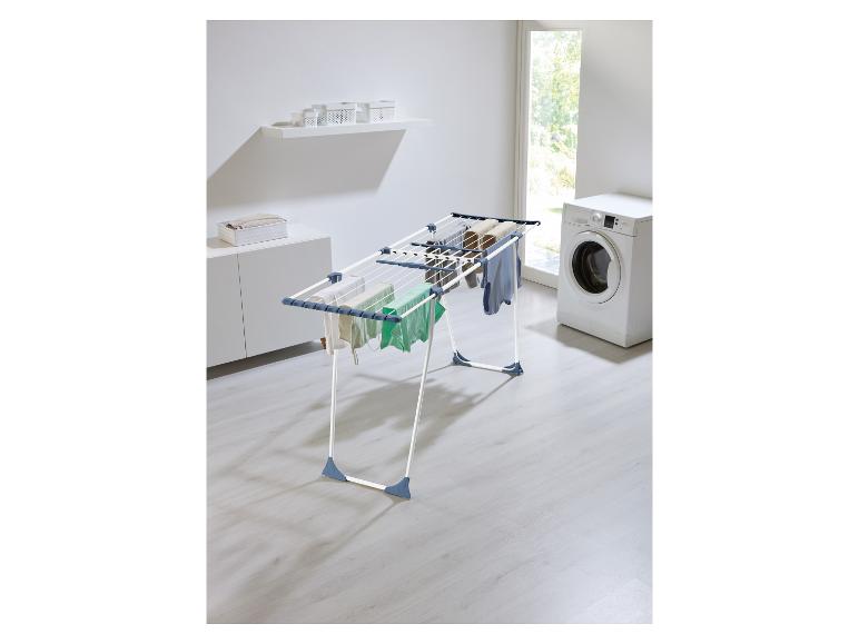 Séchoir à linge avec vêtements, machine à laver et étagères dans une buanderie lumineuse.