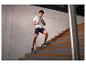 Homme en tenue de sport courant dans les escaliers, portant un t-shirt gris et un short noir.