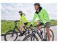 Deux personnes font du vélo, portant des vestes de sécurité fluo.