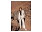 Femme en costume beige et haut noir, debout sur des rochers.