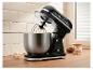 Robot pâtissier noir avec bol en acier inoxydable, œufs et amandes sur un comptoir en bois.