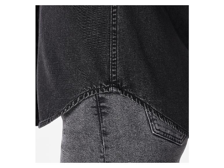 Détail d'une chemise en jean noir sur un jean foncé.