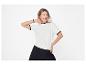 Femme souriante en t-shirt blanc à col rond et pantalon noir, posant sur fond blanc.