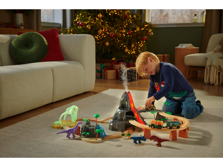 Enfant jouant avec un train et des dinosaures dans un salon de Noël.