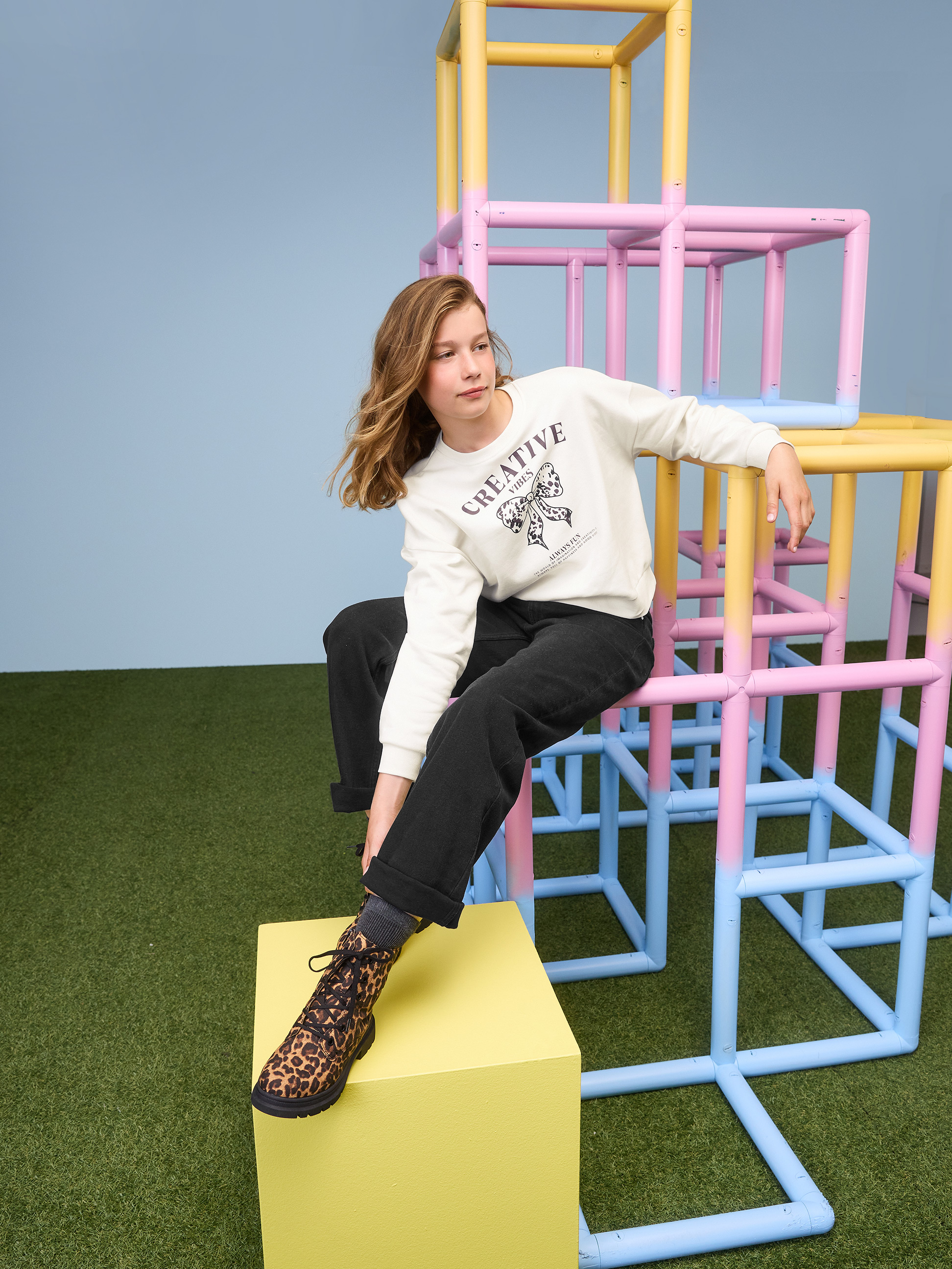 Fille en sweat blanc Creative Vibes et pantalon noir sur une structure d'escalade.