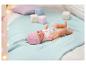 Une poupée Baby Born avec un bonnet rose et une sucette est allongée sur une couverture bleue.