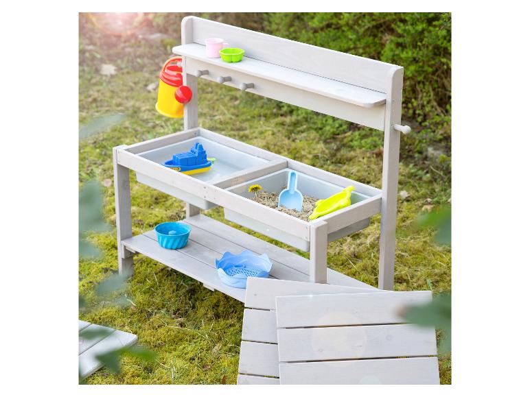 Table de jeu en bois pour sable et eau avec accessoires colorés dans un jardin.