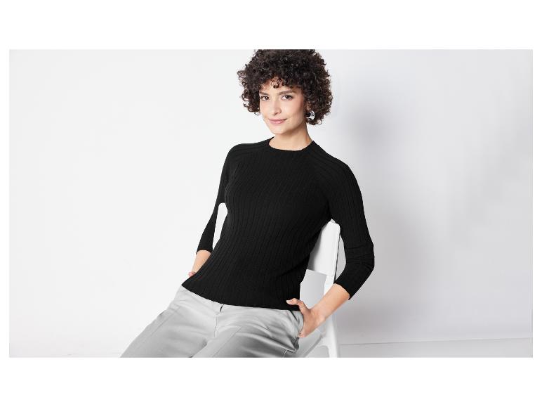 Une femme portant un pull noir à manches longues et un pantalon gris.