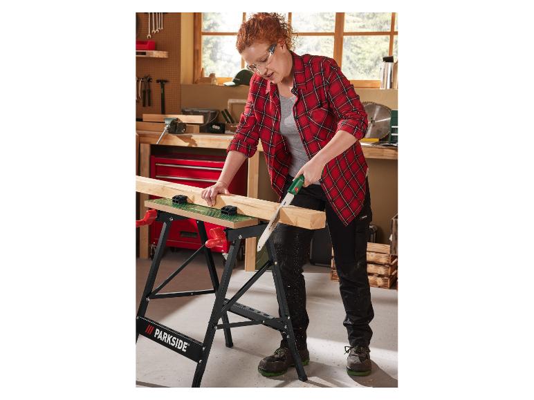 Une femme utilise une scie à main Parkside pour couper du bois sur un établi.