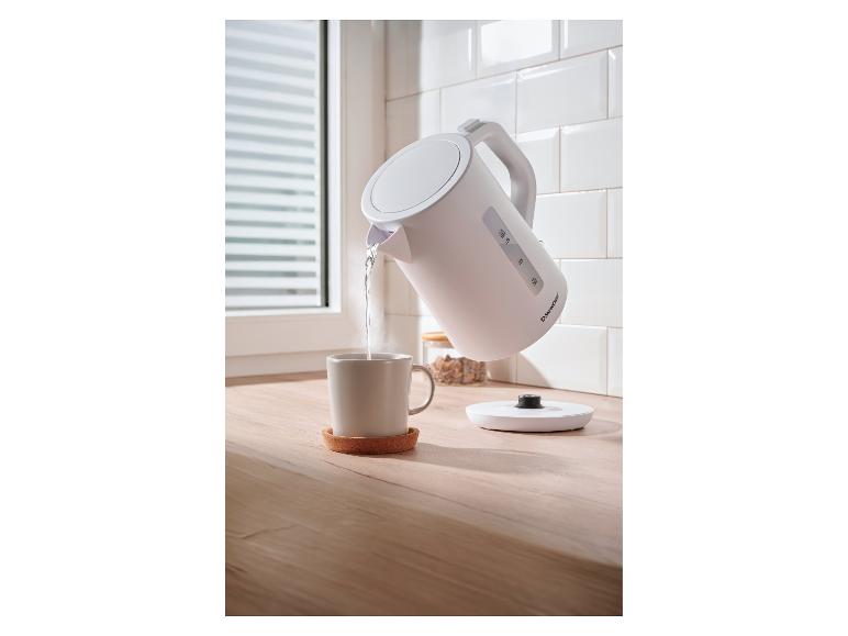 Bouilloire SilverCrest versant de l'eau chaude dans une tasse sur un comptoir en bois.