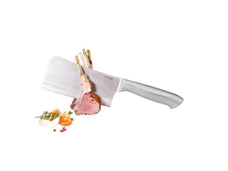 Un couperet de cuisine avec un morceau de viande, des tomates, de l'ail et des herbes.