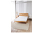 Un lit avec un cadre en bois, un matelas et un tapis dans une pièce claire.