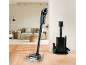 Aspirateur balai sans fil nettoyant un parquet, avec une station de charge à proximité.