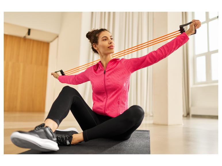 Femme en veste rose et leggings noirs faisant de l'exercice avec une bande de résistance orange.