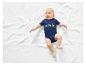 Un bébé allongé sur une couverture blanche portant un body bleu avec des dinosaures.