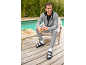 Homme en survêtement gris et sandales noires avec chaussettes blanches, souriant et tenant un smoothie vert.