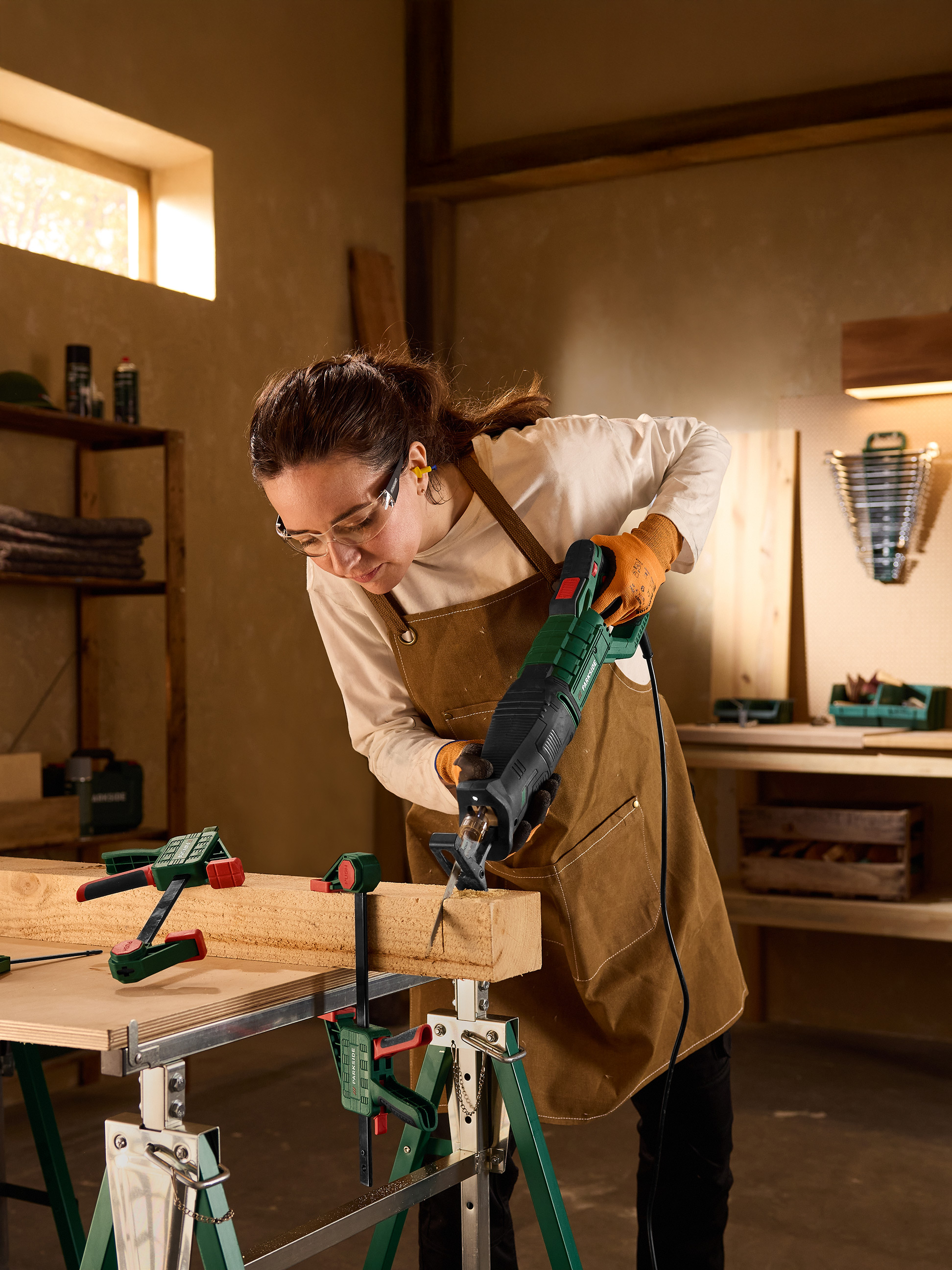 Femme utilisant une scie sabre pour couper une planche de bois, fixée par des serre-joints.