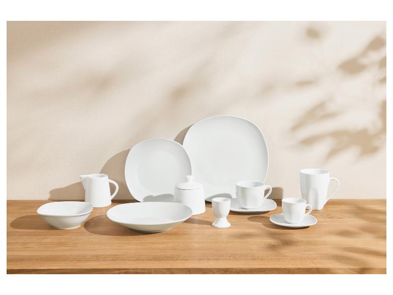 Service de table en porcelaine blanche avec assiettes, bols, tasses et pièces de service sur une table en bois.