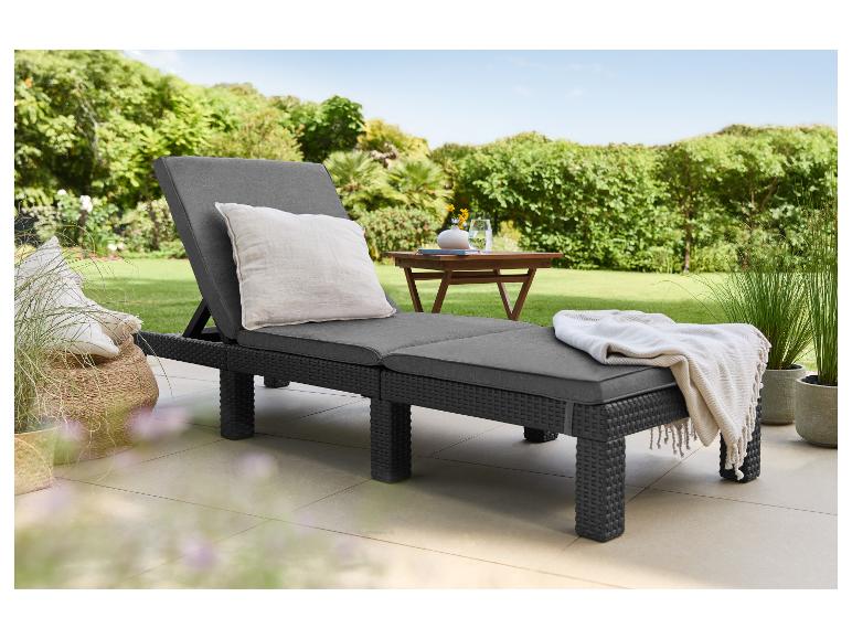 Transat gris foncé avec coussins et couverture sur une terrasse avec jardin en arrière-plan.