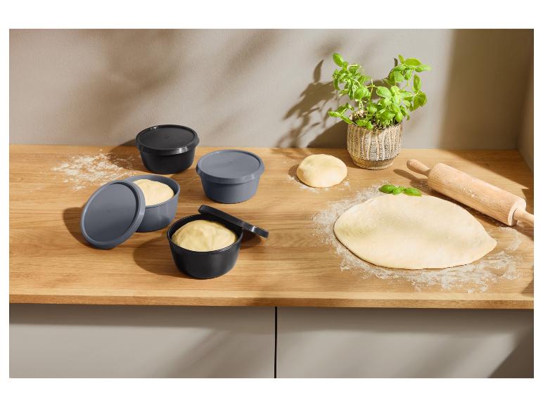 Récipients à pâte avec couvercles, pâte étalée avec de la farine et un rouleau à pâtisserie en bois sur un comptoir en bois.