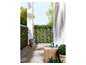 Hedges artificielles vertes avec une table de jardin en bois sur une terrasse.