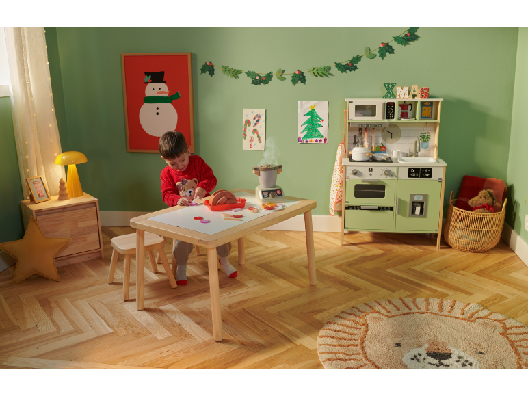 Enfant jouant avec une cuisine de jouet en bois et de la nourriture de jeu dans une pièce décorée pour Noël.