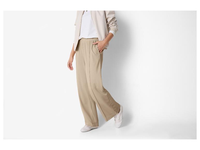 Femme en pantalon beige et t-shirt blanc avec une veste beige