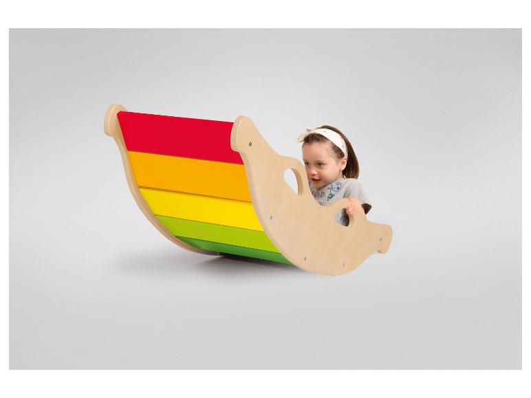 Un enfant joue sur une balançoire en bois en forme de bateau avec des rayures colorées.