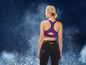 Une femme porte un soutien-gorge de sport violet et un legging noir.