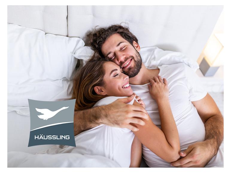 Un couple s'embrassant dans un lit avec des draps blancs, avec le logo Häussling.