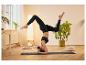 Une femme faisant du yoga sur un tapis noir avec un coussin de méditation blanc.
