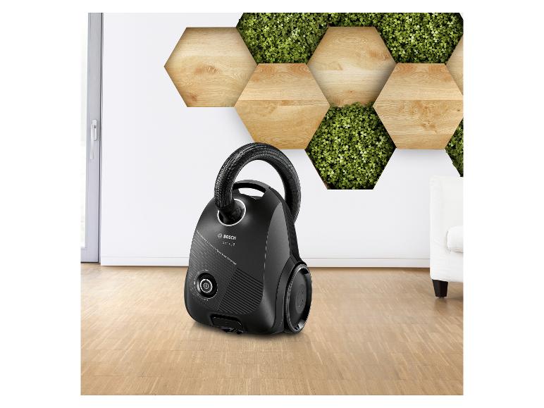 Aspirateur noir sur un parquet avec un mur décoratif en bois et plantes.