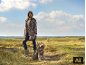 Femme en manteau léopard et chien assorti dans un champ.