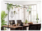 Une table à manger avec des chaises en rotin et une étagère décorative avec des plantes suspendues et des lumières.