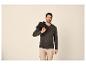 Homme en chemise henley vert foncé et pantalon cargo beige, avec une veste sur l'épaule.