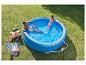 Couple se relaxant dans une piscine gonflable bleue, avec chaises longues et serviettes sur l'herbe.