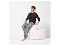 Homme en t-shirt noir à manches longues et pantalon à carreaux gris, assis sur un pouf blanc.