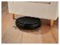 Aspirateur robot noir sous un canapé beige sur un parquet.